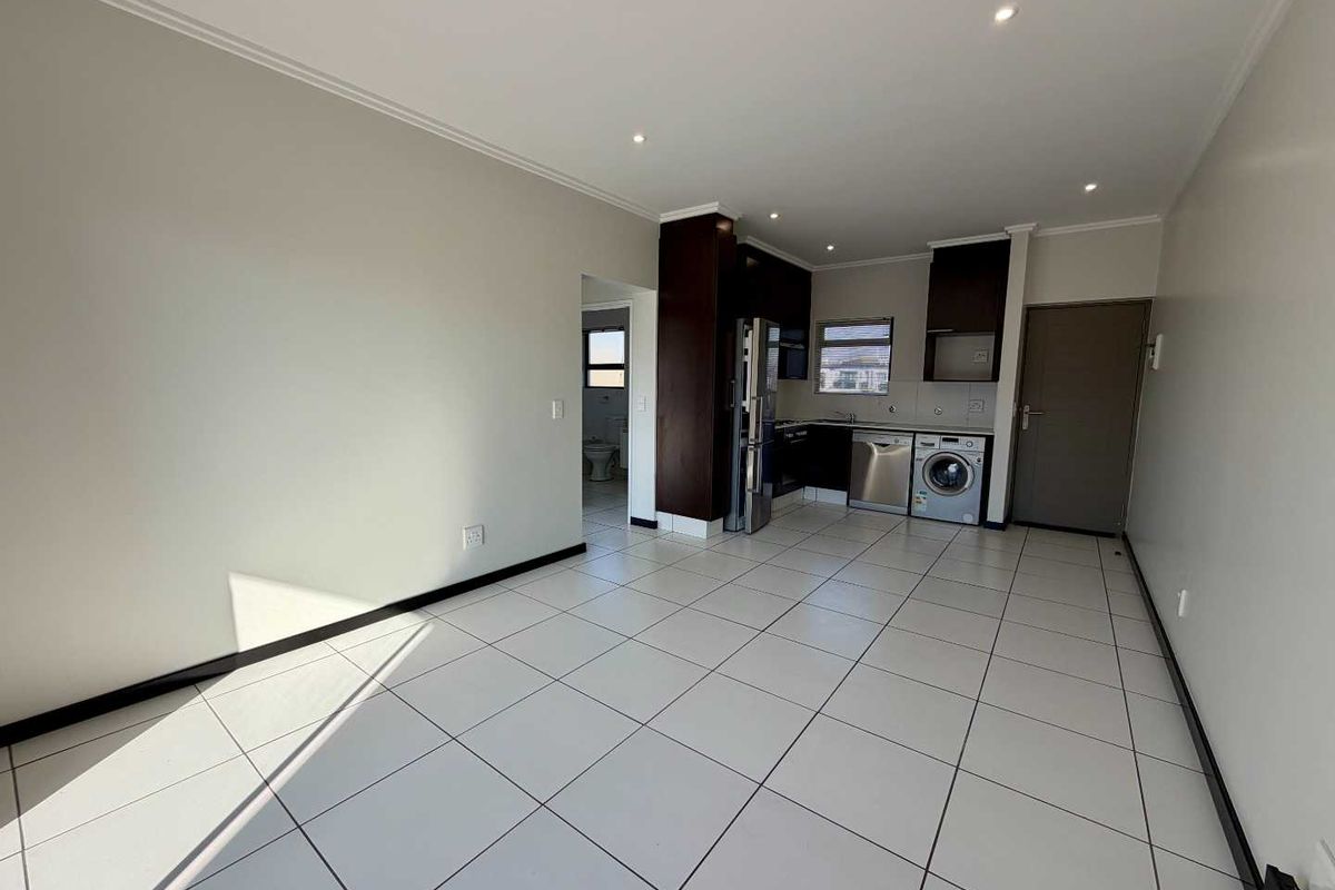 An open-plan living and kitchen area featuring tiled flooring, recessed lighting, and modern built-in cabinetry with integrated appliances.