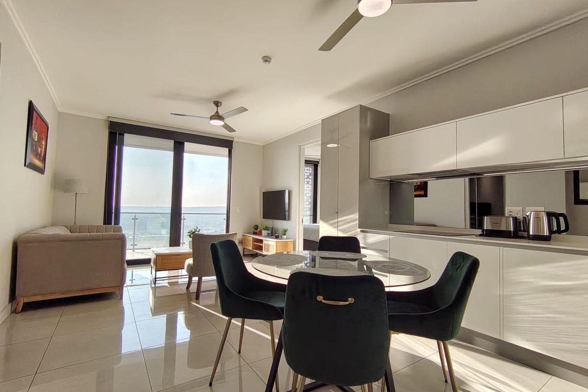 Modern open-plan living and dining area featuring sleek kitchen cabinetry, tiled floors, ceiling fans, and a sliding door leading to a balcony with views.