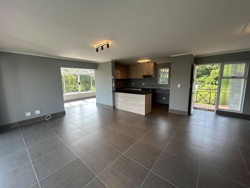 Spacious open-plan living area featuring modern tiled floors, a functional kitchen with built-in cabinetry, and direct access to a private balcony.