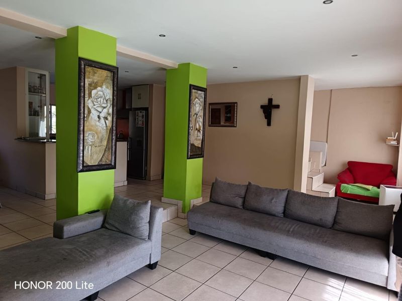 Open plan living area featuring ceramic floor tiles, recessed lighting, and structural columns, connecting to a kitchen space.