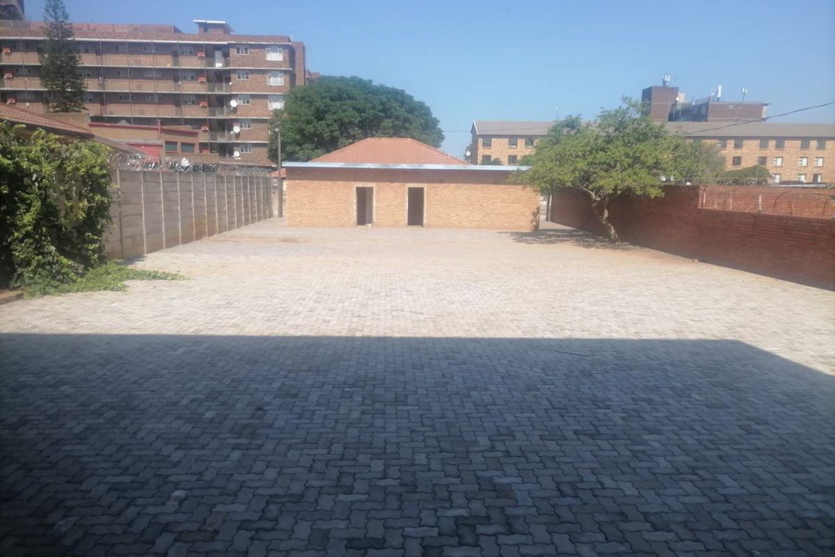 A spacious industrial yard featuring extensive paved surfacing, enclosed by perimeter brick walls and security fencing, providing ample open-air utility space.