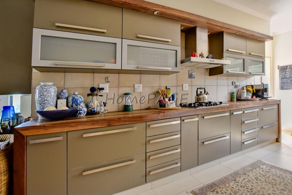 Modern kitchen featuring sleek cabinetry, a warm wooden countertop, integrated gas hob, stainless steel extractor fan, and neutral tiled backsplash.