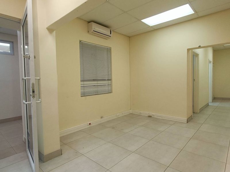 A vacant office space featuring tiled flooring, a drop ceiling with recessed lighting, and a wall-mounted air conditioning unit.