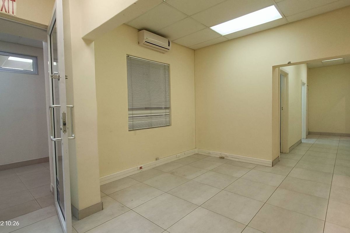 A vacant office space featuring tiled flooring, a drop ceiling with recessed lighting, and a wall-mounted air conditioning unit.