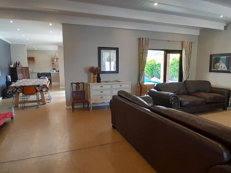 Spacious open-plan living and dining area featuring polished concrete floors, exposed ceiling beams, and direct access to the outdoor pool area.
