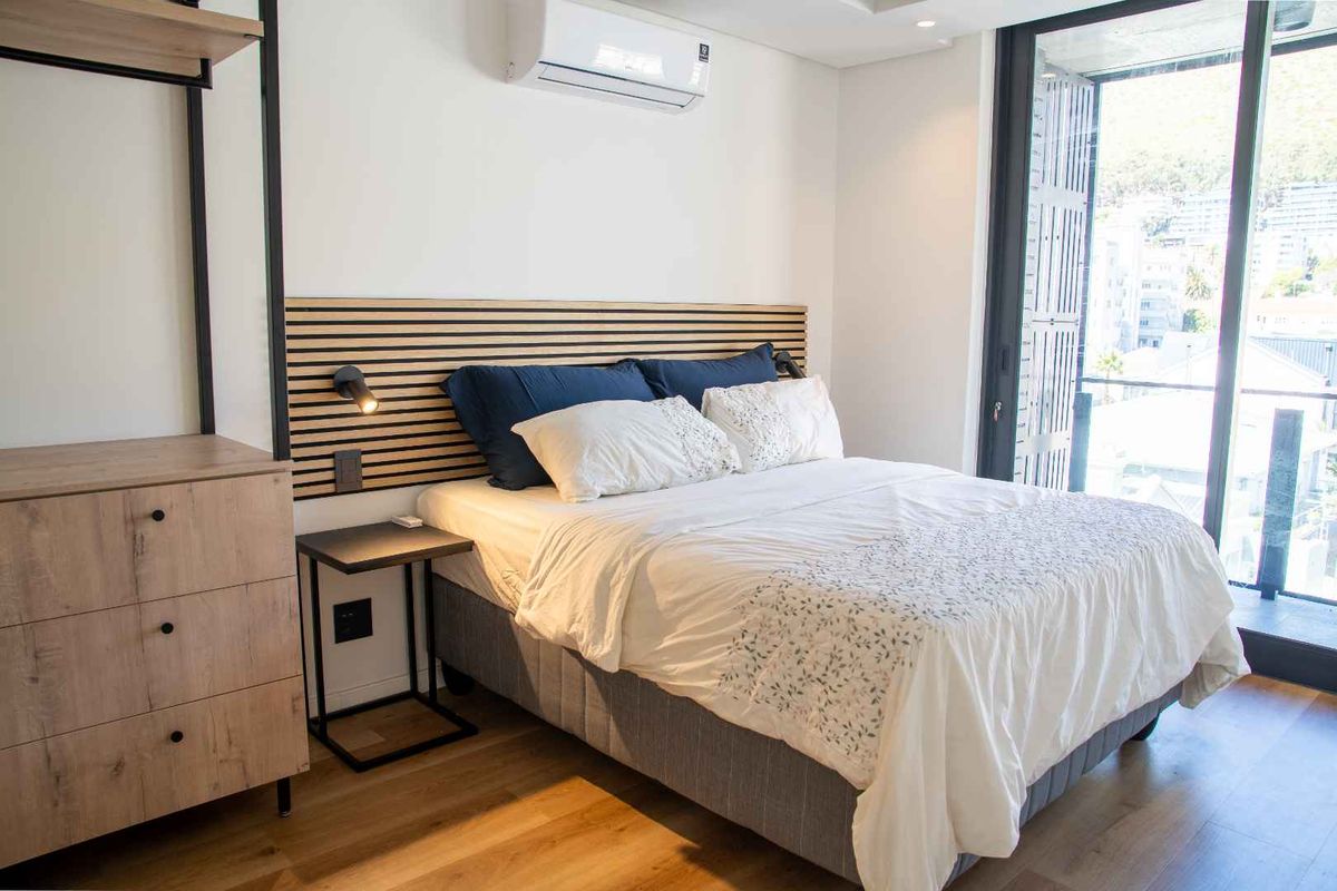 Modern bedroom featuring timber slat headboard detail, split-system air conditioning unit, and large sliding glass doors opening to a private balcony.