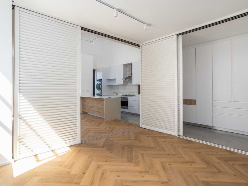 Modern open-plan living area featuring herringbone timber flooring, sliding louvered partitions, and a sleek, well-appointed kitchen with stone island and integrated appliances.