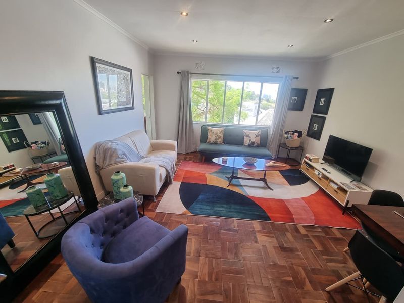 A bright and inviting living room featuring classic parquet flooring and recessed downlights, offering a comfortable space with natural light.