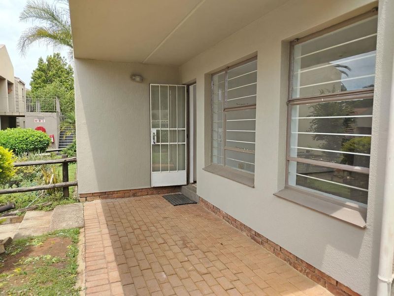 A covered patio area featuring brick paving, a security gate, and windows fitted with burglar bars, providing direct access to the exterior.