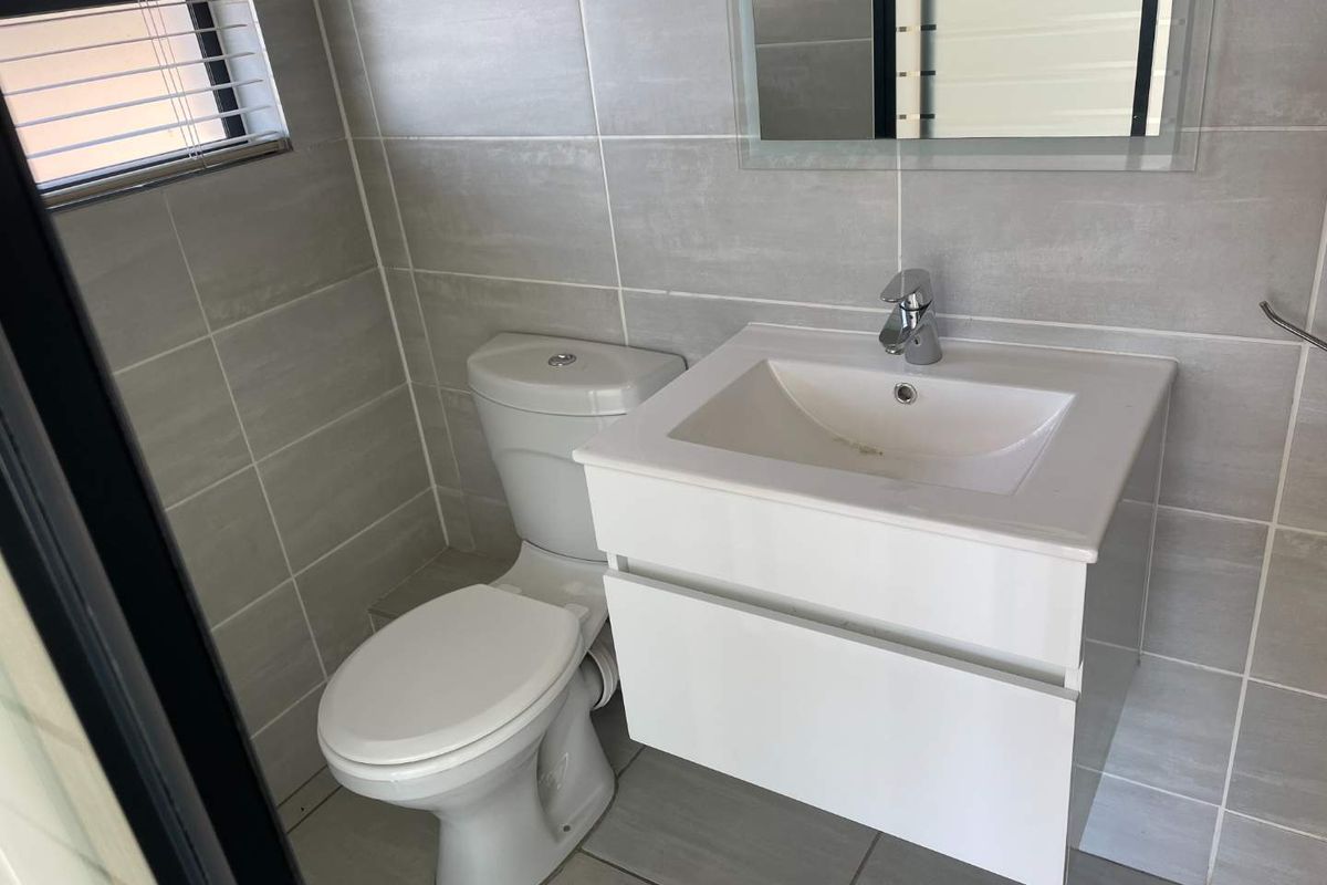 A modern bathroom featuring grey wall and floor tiles, a white vanity with a basin, and a standard toilet.