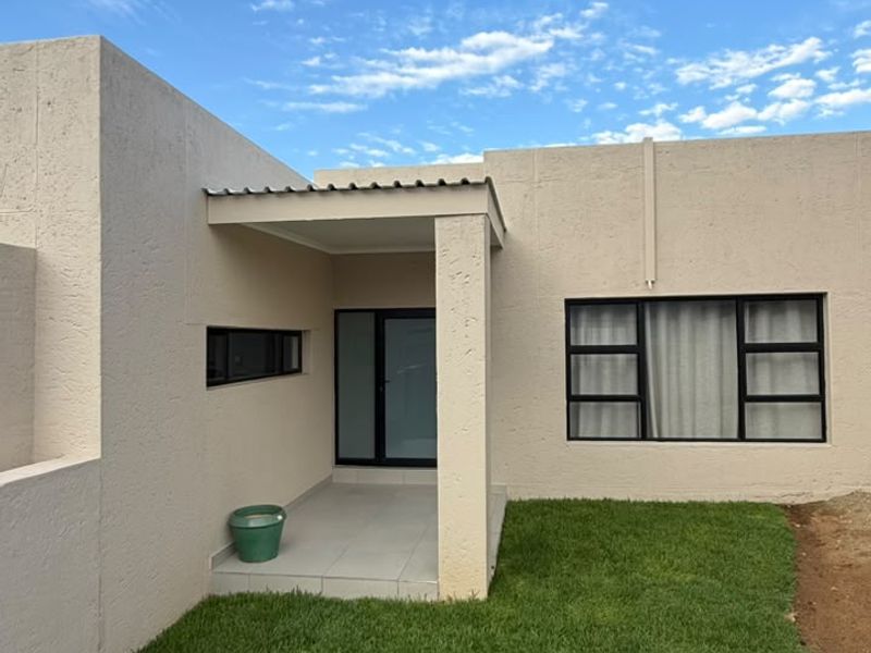 A well-maintained rear exterior view featuring a covered patio, neat lawn, and modern black aluminium window frames against a textured facade.