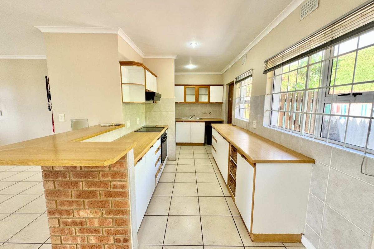 A functional kitchen featuring a brick-base breakfast bar, wooden countertops, built-in cabinetry, and tiled flooring with ample natural light.