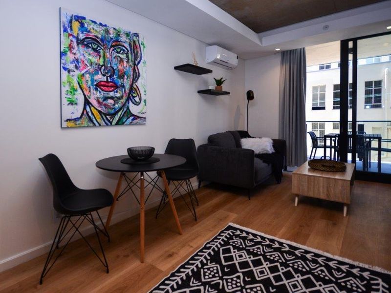 Modern living area featuring hardwood flooring, recessed ceiling detail, and direct access to a private balcony through sliding glass doors.
