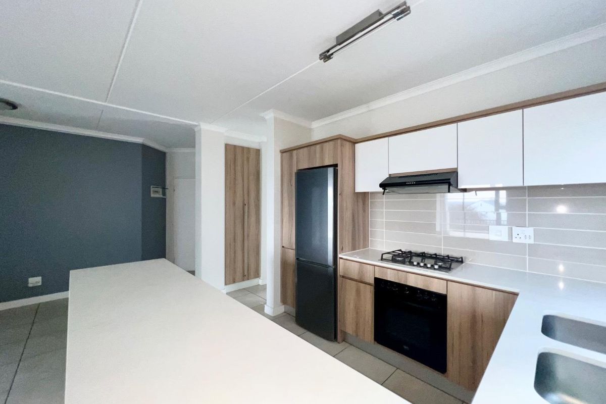 Modern kitchen featuring wood-grain and white cabinetry, stone countertops, a gas hob, built-in oven, extractor fan, and a double sink.