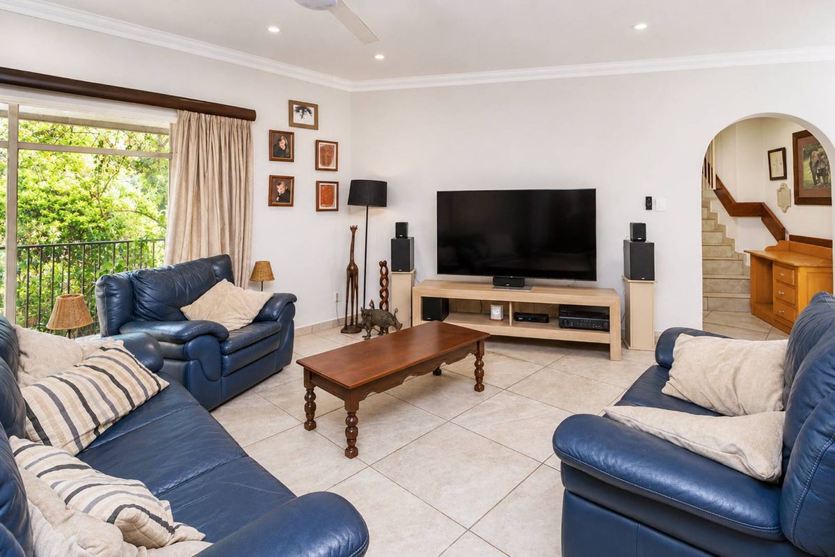Spacious living room featuring neutral tiled flooring, recessed lighting, and an arched entryway leading to a staircase, with access to a balcony.