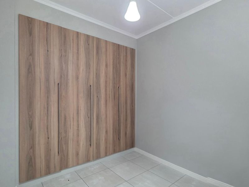 A clean, empty bedroom featuring modern wood-finish built-in cupboards and neutral tiled flooring, providing a versatile space ready for personalization.