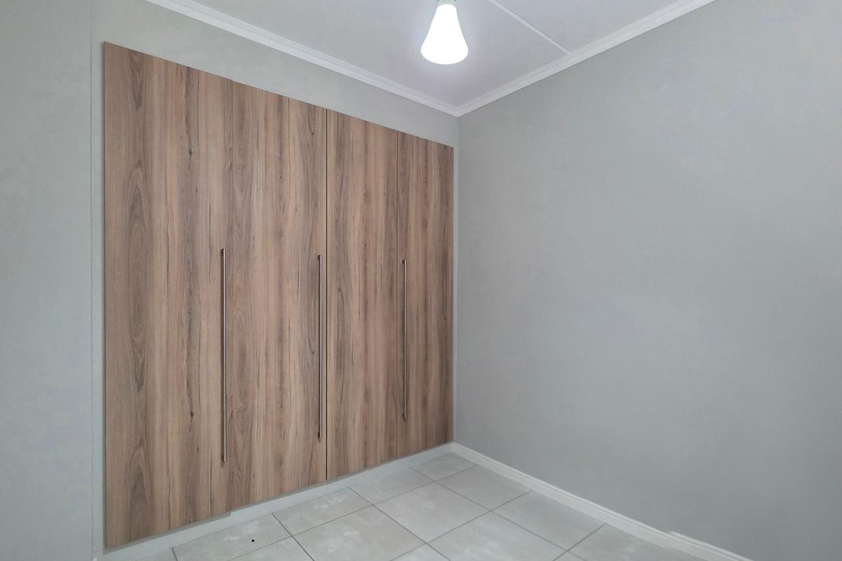 A clean, empty bedroom featuring modern wood-finish built-in cupboards and neutral tiled flooring, providing a versatile space ready for personalization.
