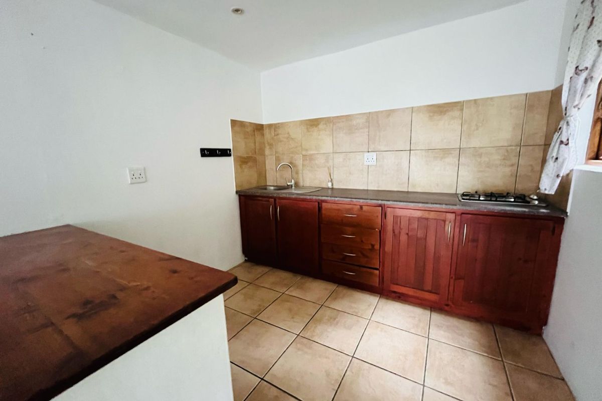 A functional kitchen featuring wooden cabinetry, tiled backsplash, integrated gas hob, and a stainless steel sink with tiled flooring.