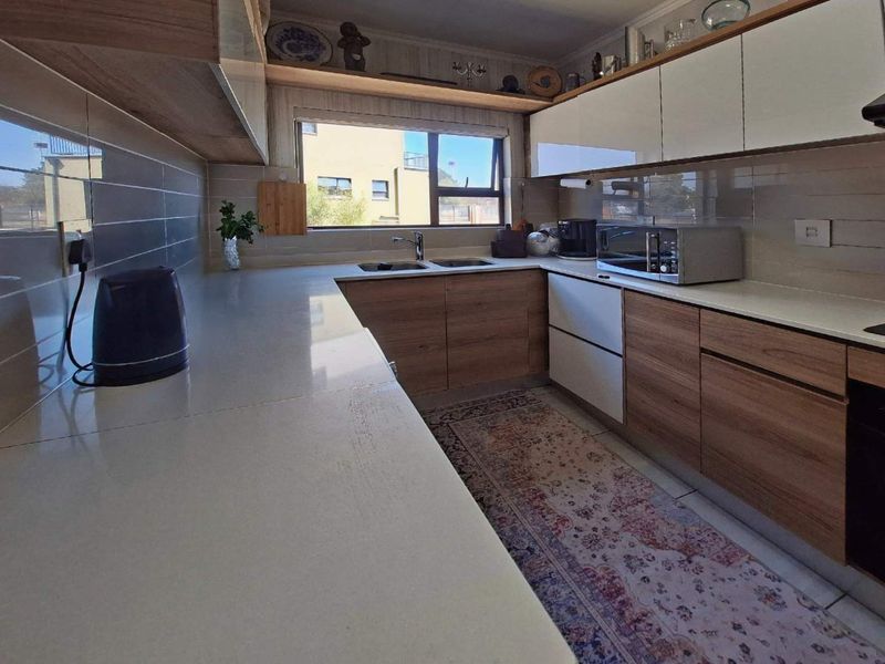 Modern kitchen featuring wood-grain and white cabinetry, quartz countertops, a double basin sink, and a tiled backsplash with ample storage space.