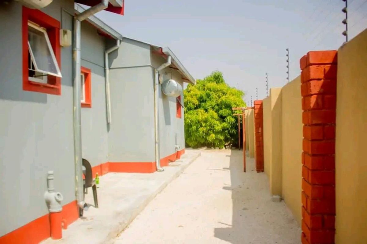 Side exterior view of the house featuring a paved walkway, perimeter boundary wall with electric fencing, and external plumbing fixtures.