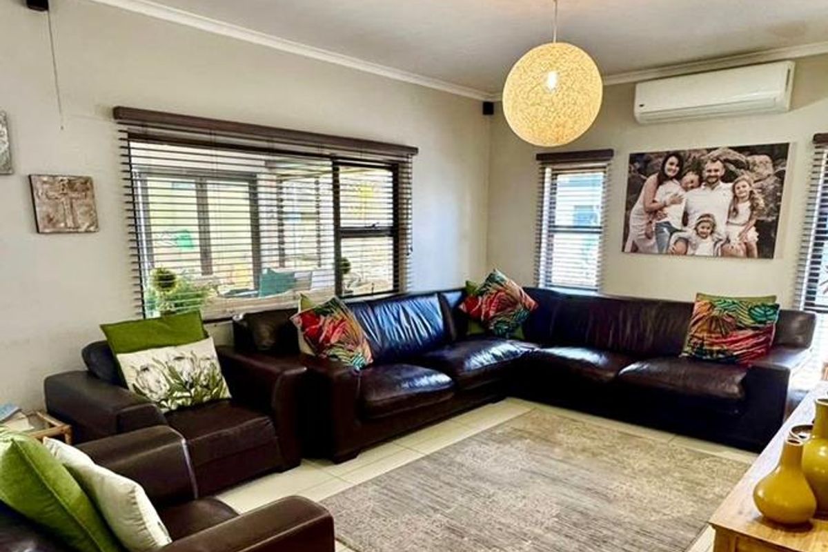 A comfortable living room featuring large format floor tiles, a wall-mounted air conditioning unit, and venetian blinds on the windows.