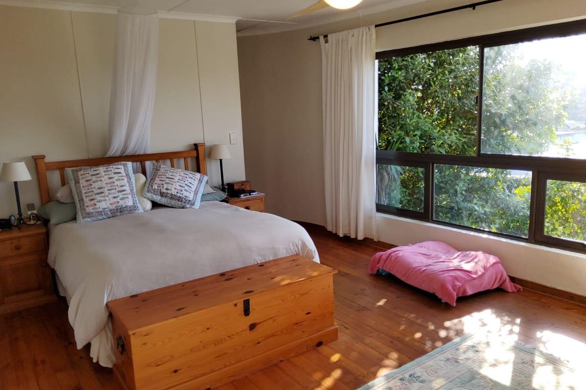 A spacious bedroom featuring warm timber flooring and a large sliding window that provides ample natural light and views of the surrounding greenery.