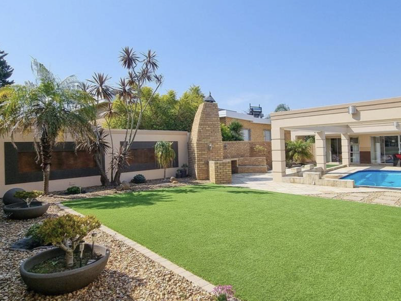 Well-maintained outdoor entertainment area featuring a swimming pool, covered patio, and a built-in brick braai set within a landscaped garden.