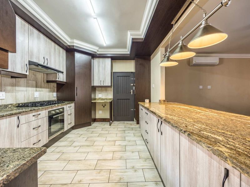 Modern kitchen featuring granite countertops, built-in oven, gas hob, extractor fan, and ample cabinetry with a coved ceiling and integrated lighting.