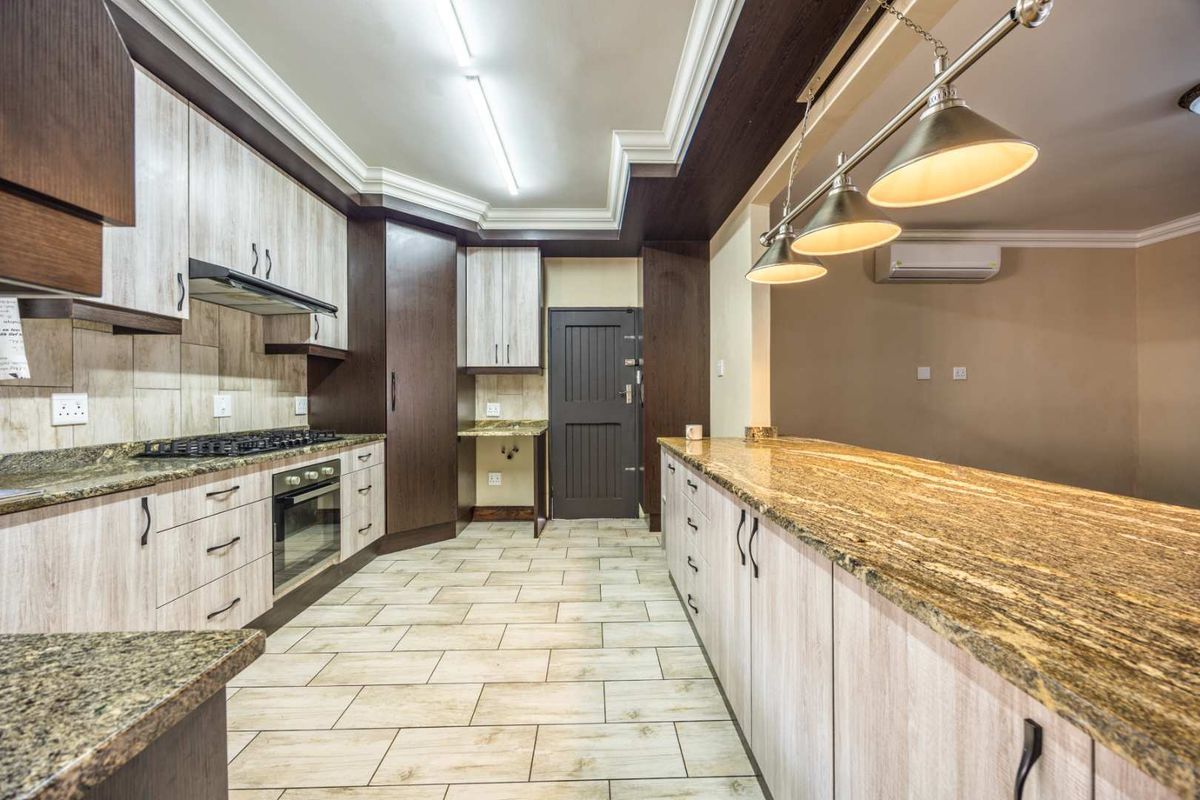 Modern kitchen featuring granite countertops, built-in oven, gas hob, extractor fan, and ample cabinetry with a coved ceiling and integrated lighting.