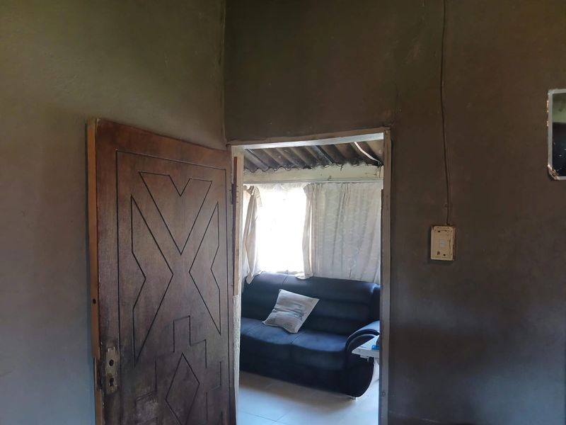 Interior view showing a doorway leading into a living area with unfinished plaster walls and exposed ceiling rafters.