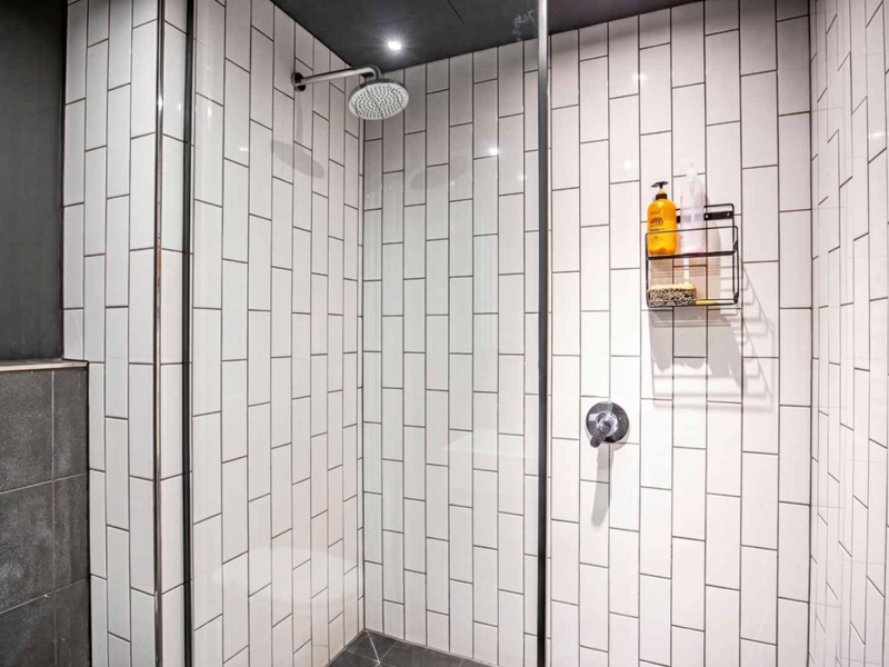 A modern walk-in shower featuring white subway wall tiles, a rainfall shower head, and a sleek glass enclosure.