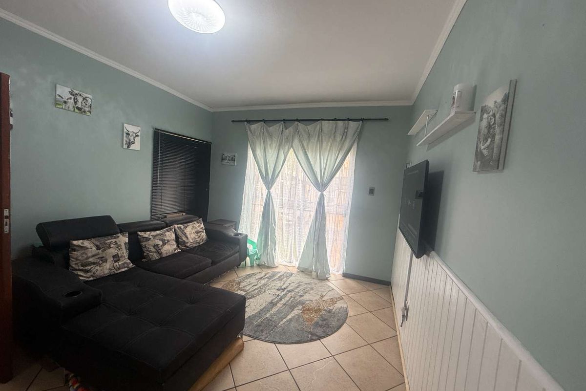 A cozy living room featuring tiled flooring, wall-mounted television, and a sliding glass door providing access to the exterior.