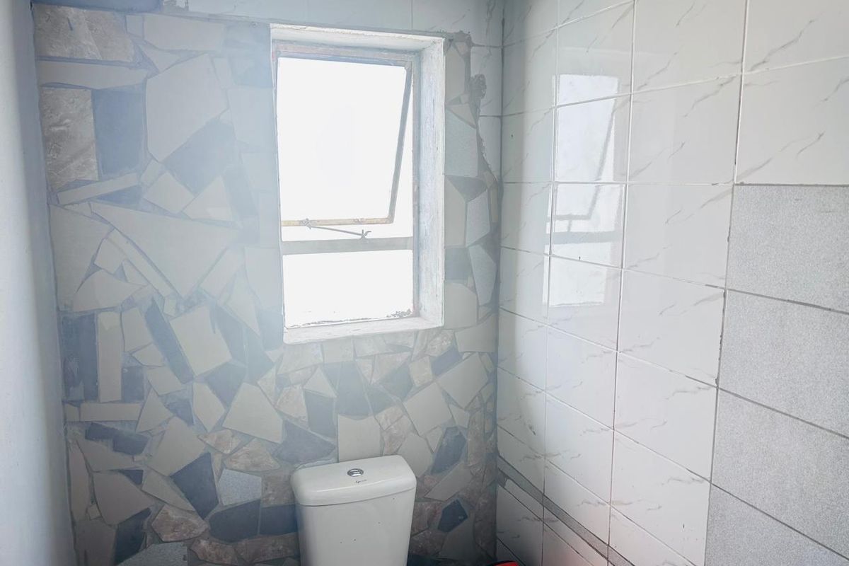 A small bathroom featuring a toilet and a mix of tiled wall finishes, currently requiring completion and cosmetic updates to the wall surfaces.