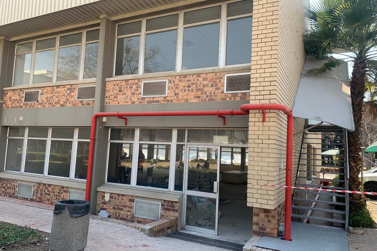 Front elevation of an industrial building featuring brick facade, large windows, external fire safety piping, and an external metal staircase.