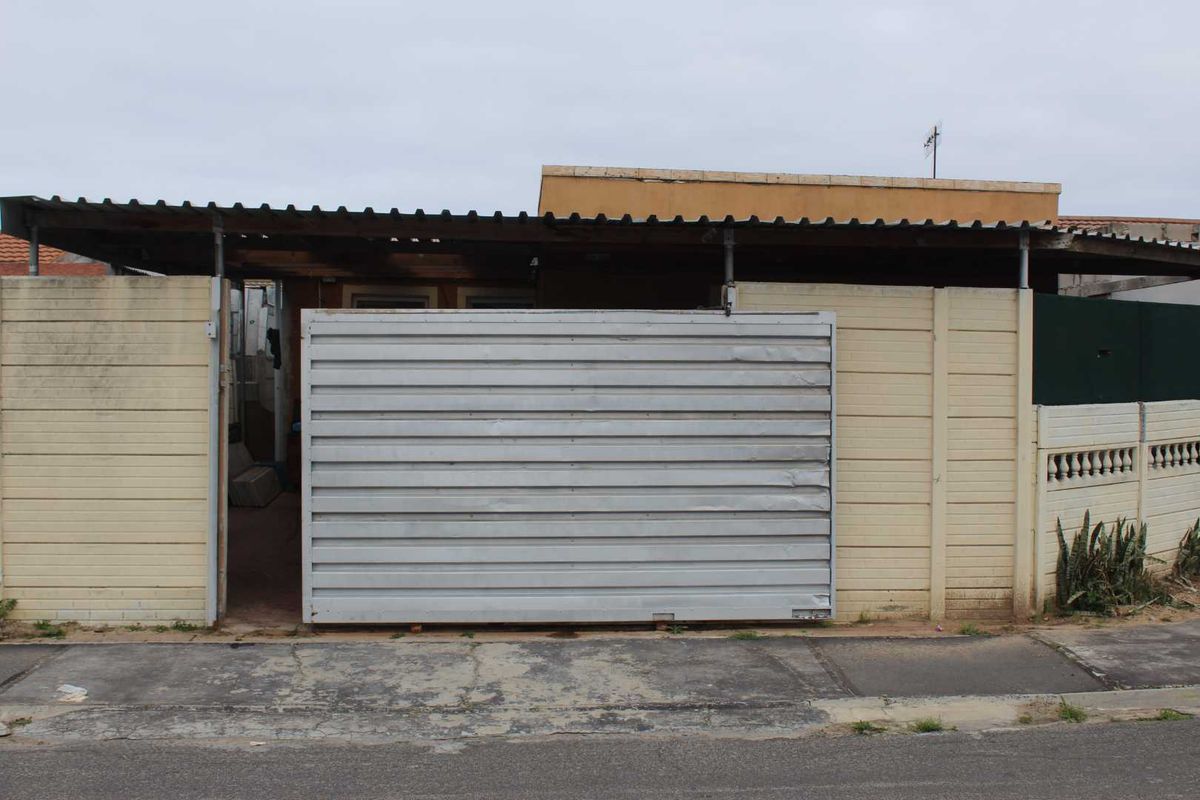 Front exterior view of the property featuring a sliding metal gate, corrugated roof covering, and precast concrete boundary walling.