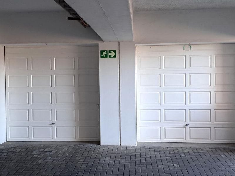 A clean and well-maintained indoor garage area featuring two white sectional garage doors and paved flooring.