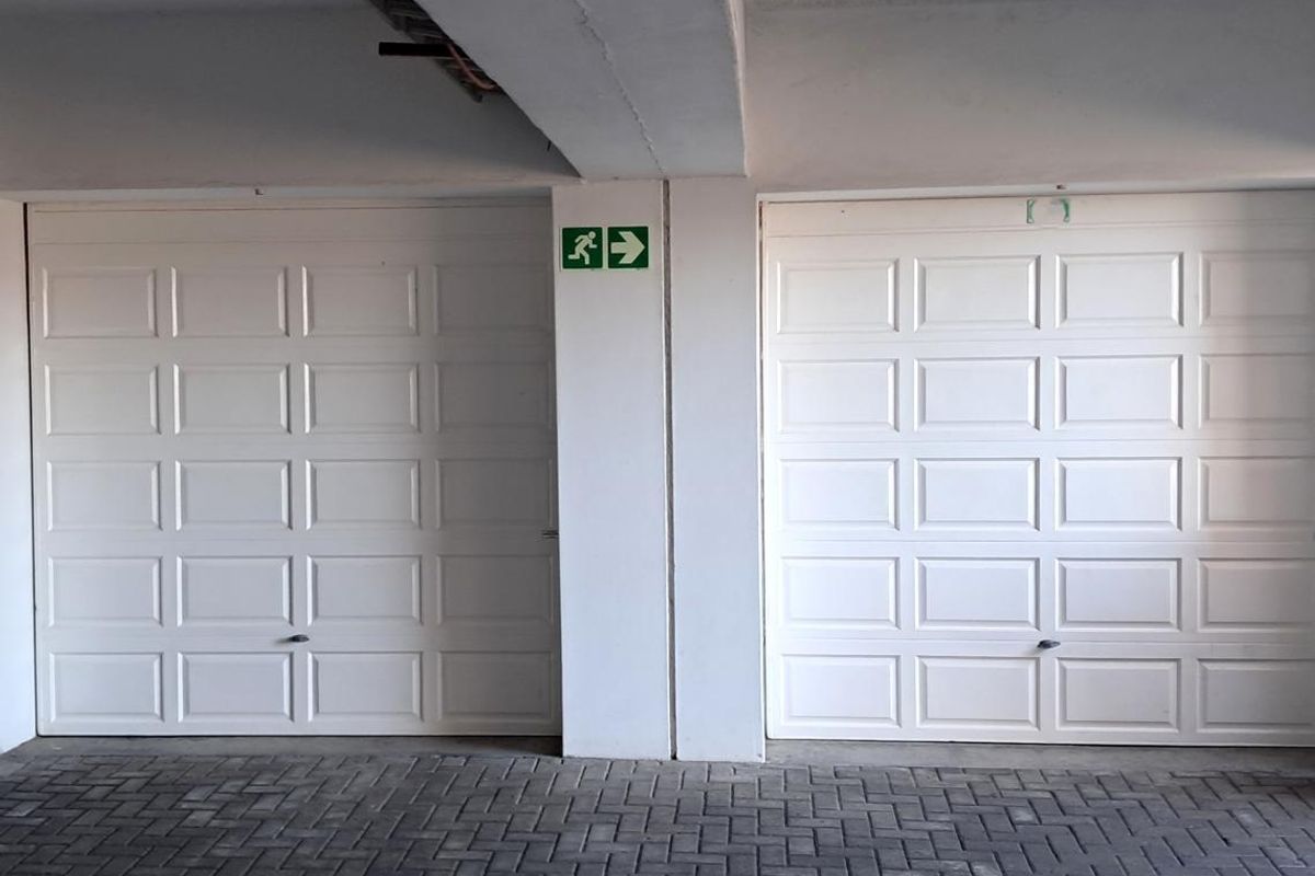 A clean and well-maintained indoor garage area featuring two white sectional garage doors and paved flooring.
