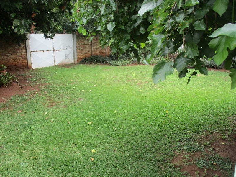 A private backyard garden featuring a grass lawn, mature trees, and a brick boundary wall with a metal gate.