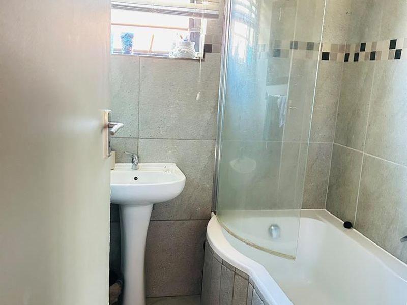 A functional bathroom featuring a pedestal basin and a shower-over-bath combination with a curved glass screen and neutral wall tiling.