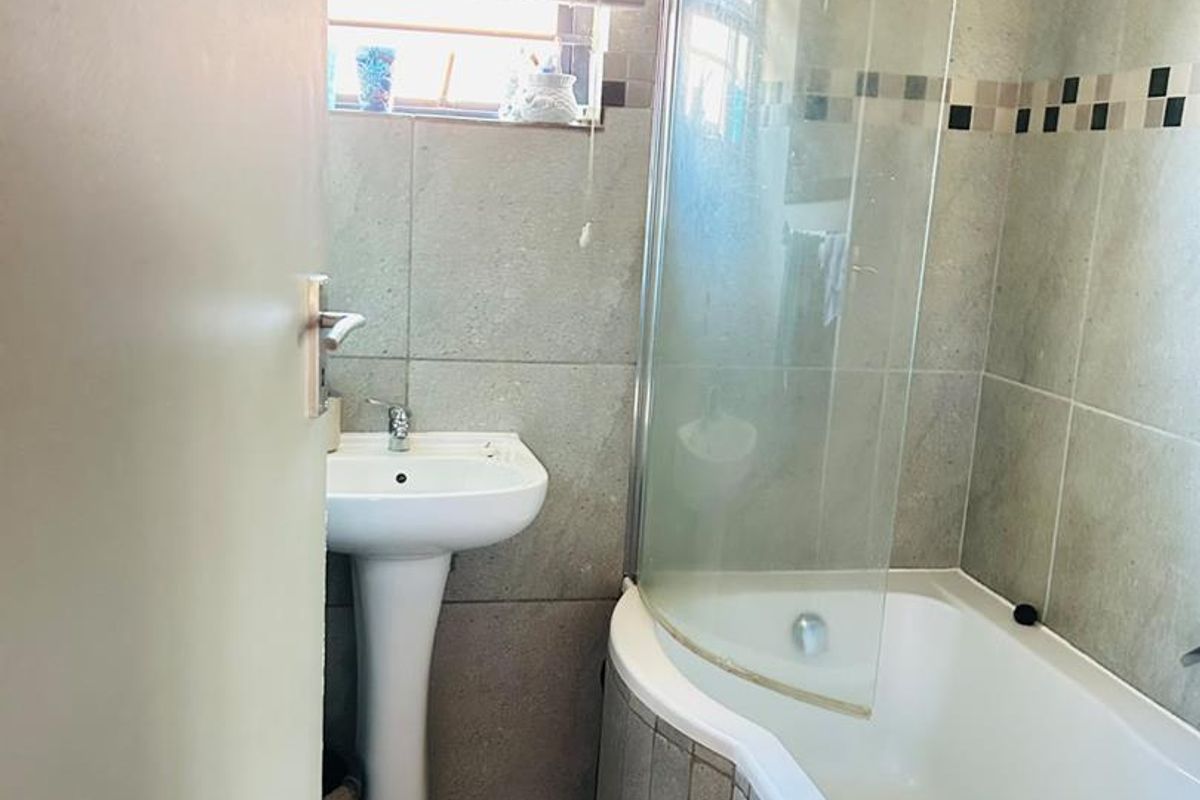A functional bathroom featuring a pedestal basin and a shower-over-bath combination with a curved glass screen and neutral wall tiling.