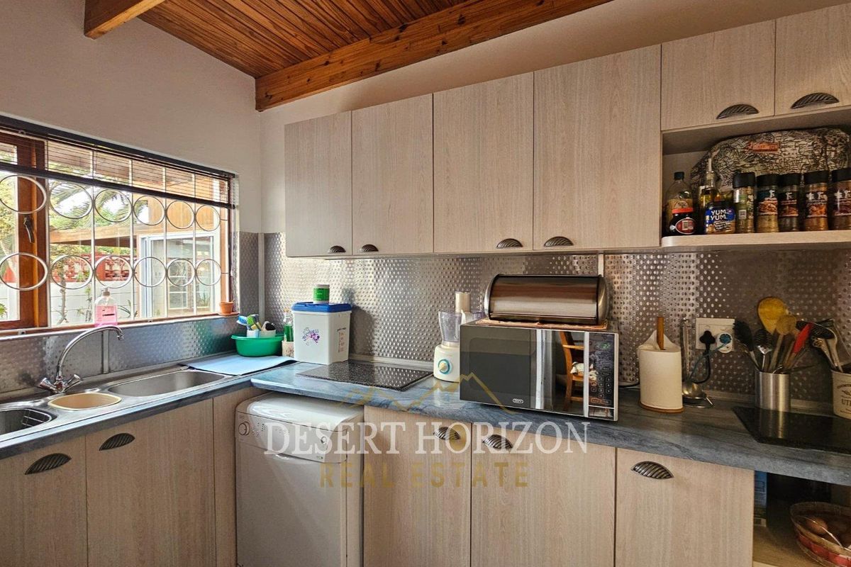 A functional kitchen featuring light wood-look cabinetry, a stainless steel splashback, double bowl sink, and a distinctive timber-paneled ceiling.