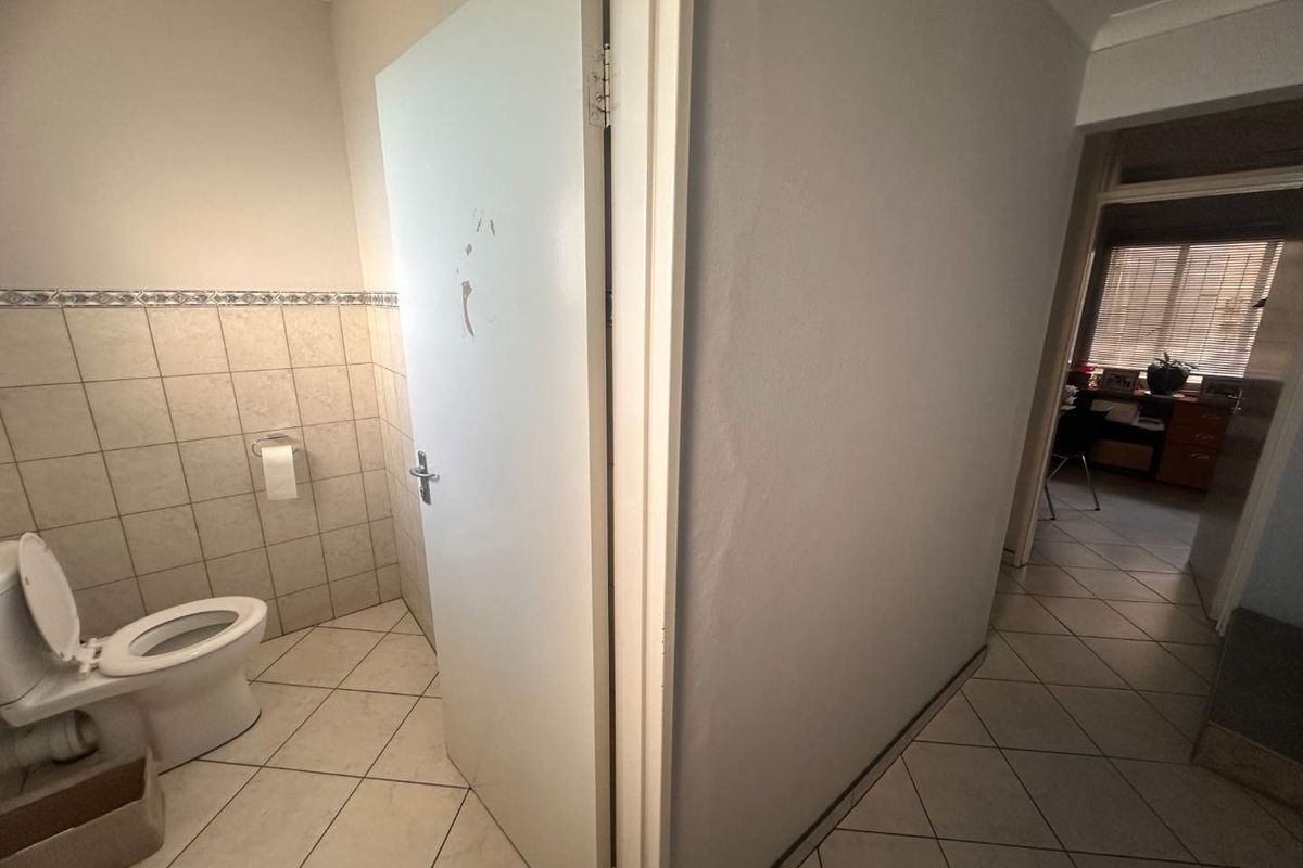 A small bathroom featuring ceramic tiling and a standard toilet, showing signs of wear on the door and wall surfaces.