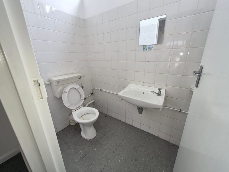 A functional, compact bathroom featuring white wall tiles, a wall-mounted basin, and a standard toilet, requiring cosmetic updates to improve its overall aesthetic.