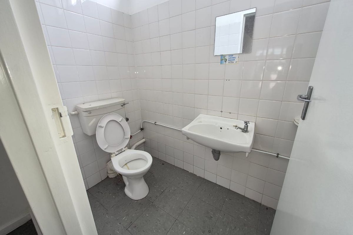 A functional, compact bathroom featuring white wall tiles, a wall-mounted basin, and a standard toilet, requiring cosmetic updates to improve its overall aesthetic.