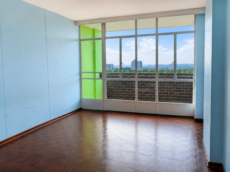 An empty living room featuring original parquet flooring, large windows with city views, and a bright accent wall.