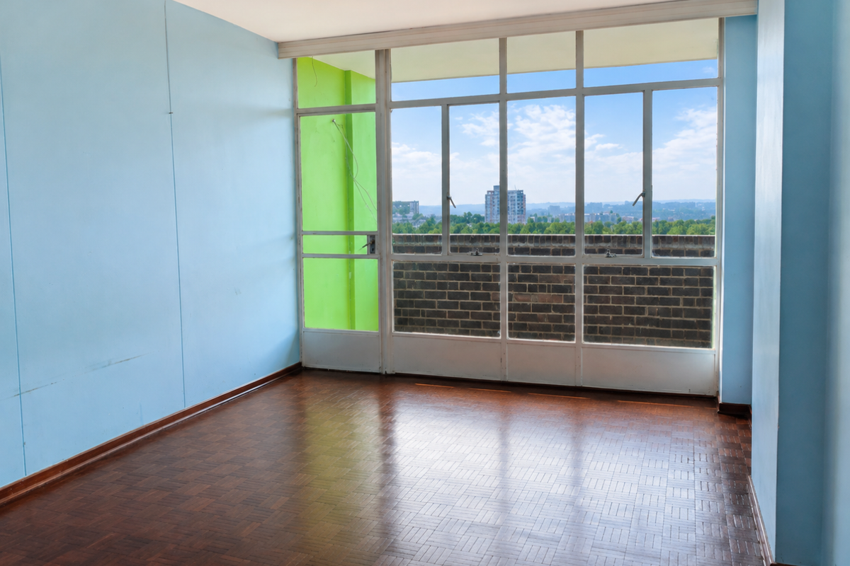 An empty living room featuring original parquet flooring, large windows with city views, and a bright accent wall.