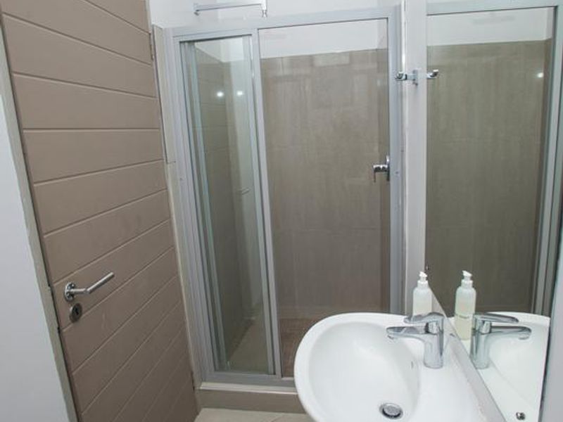 A clean and functional bathroom featuring a pedestal basin, a glass-enclosed shower, and neutral floor tiling.