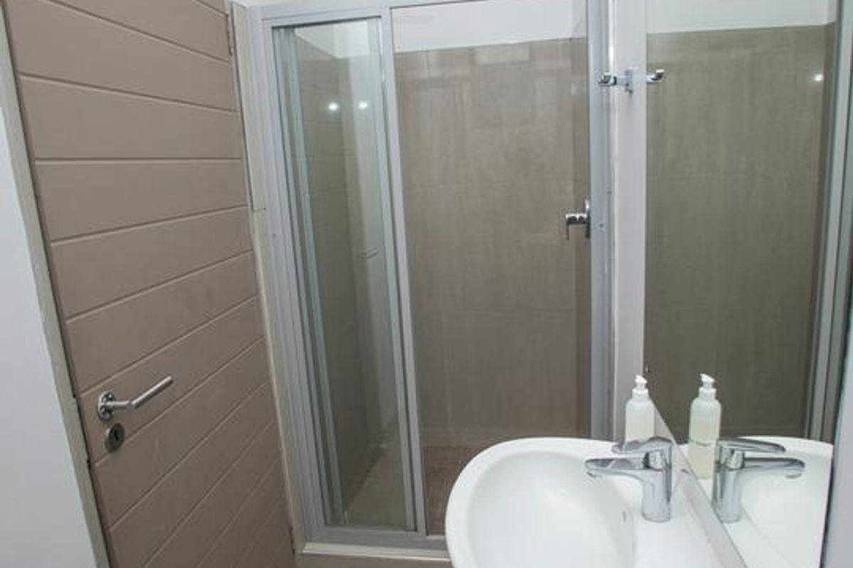 A clean and functional bathroom featuring a pedestal basin, a glass-enclosed shower, and neutral floor tiling.