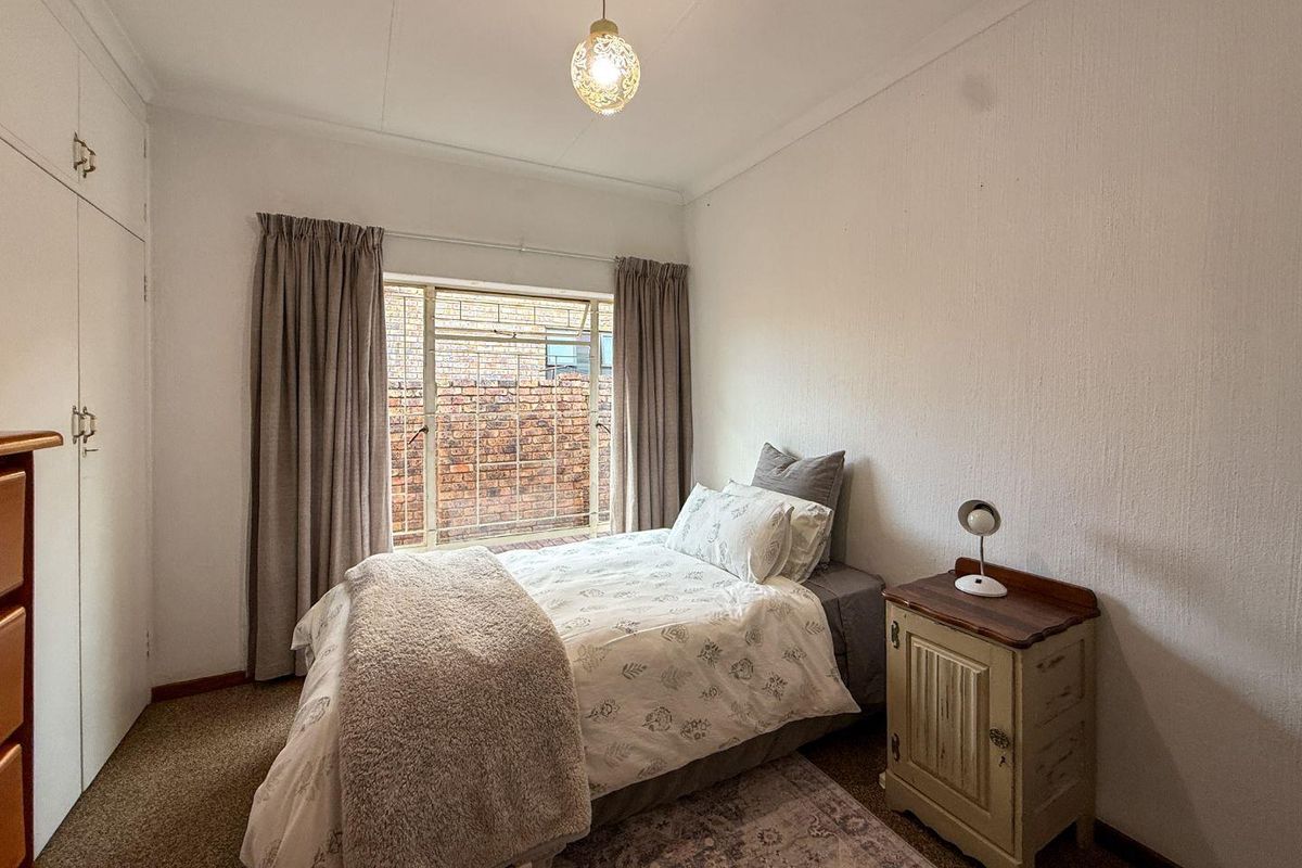 A functional bedroom featuring built-in cupboards, carpeted flooring, and a steel-framed window overlooking a brick wall.