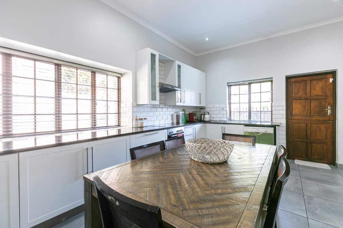 A well-lit kitchen featuring white cabinetry, granite countertops, subway tile backsplash, and integrated appliances, with a functional layout and tiled flooring.